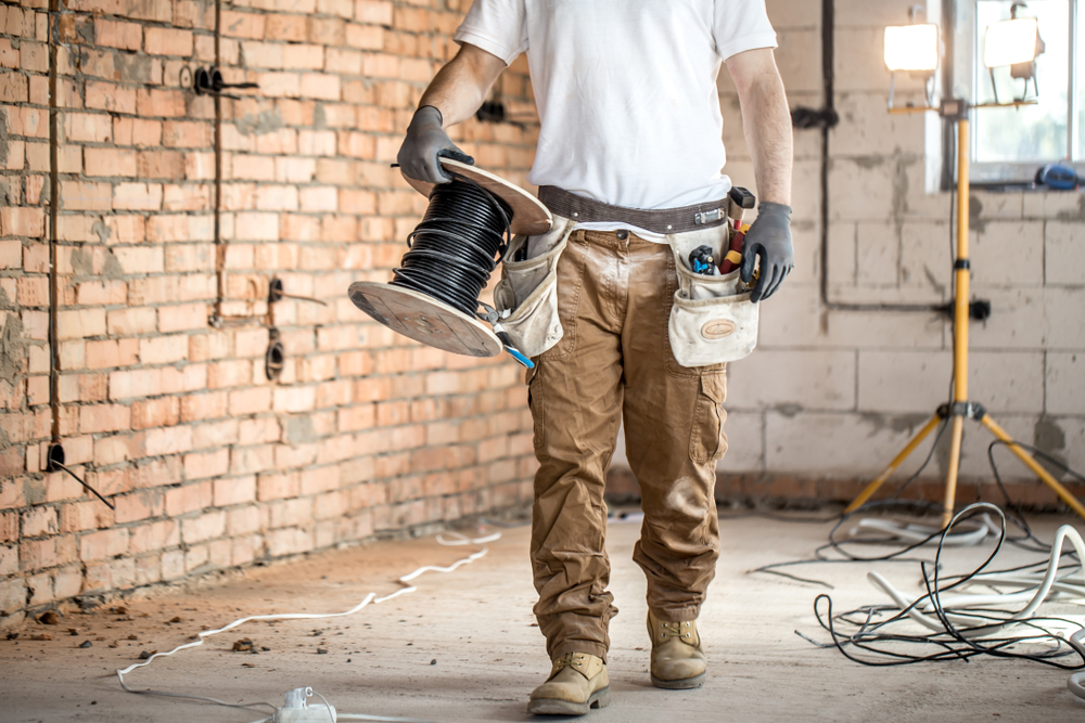 electrician carrying spool of wire through work area.